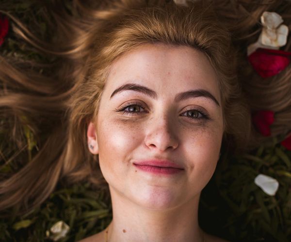 Person smiling peacefully with eyes closed in a calm, natural setting.